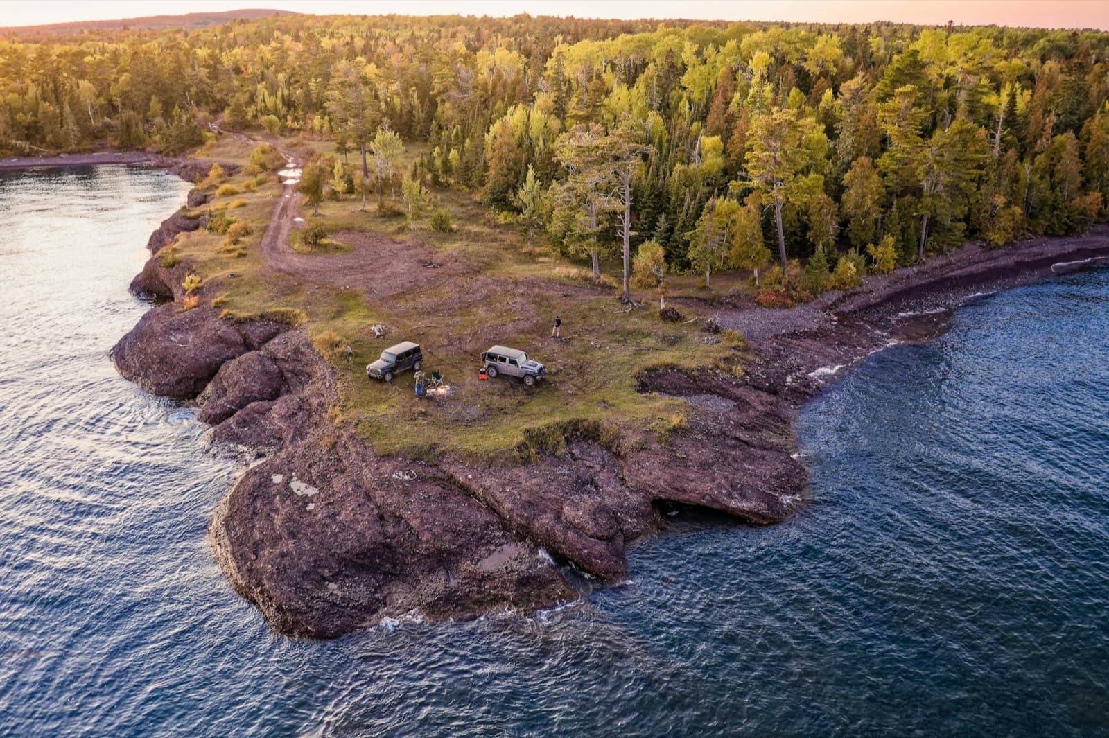 Aerial of two camper rigs on a rocky point above a lake at sunset